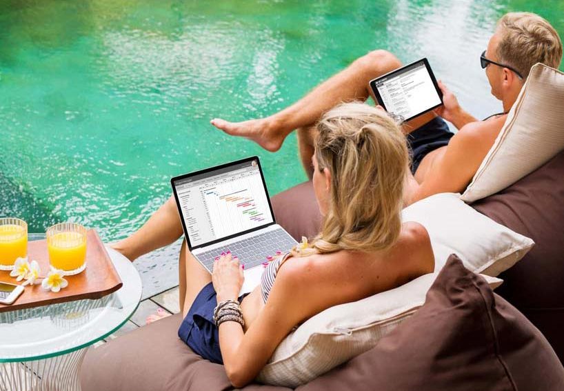 Mann und Frau sitzen zusammen am Pool vor ihren Laptops und arbeiten.
