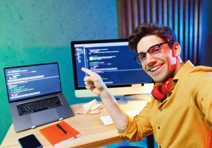 Softwaretester sitzt vor einem Laptop und einem Computer und testet die Software.